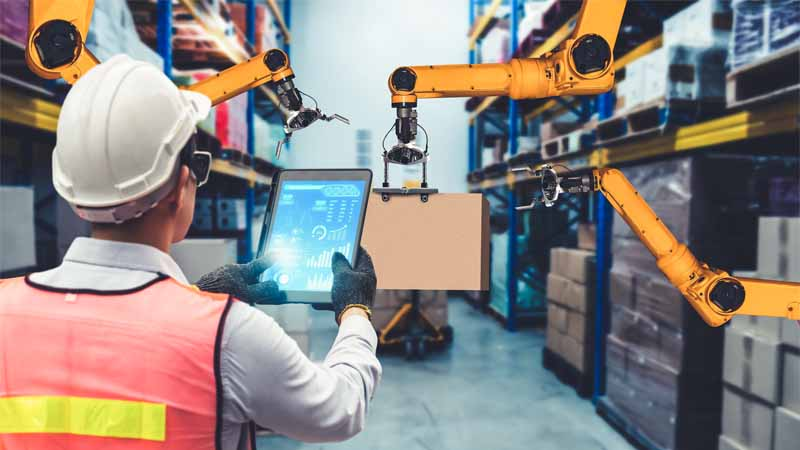 A warehouse worker beside automated robotic equipment.